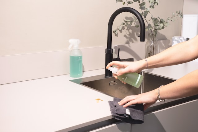 Hands wiping down a counter and sink with a spray bottle and towel